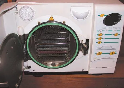 Fig 4. Small benchtop steam steriliser (autoclave) with the door open, showing loaded instrument trays and a vacuum plus rapid-sterilisation cycle control panel.